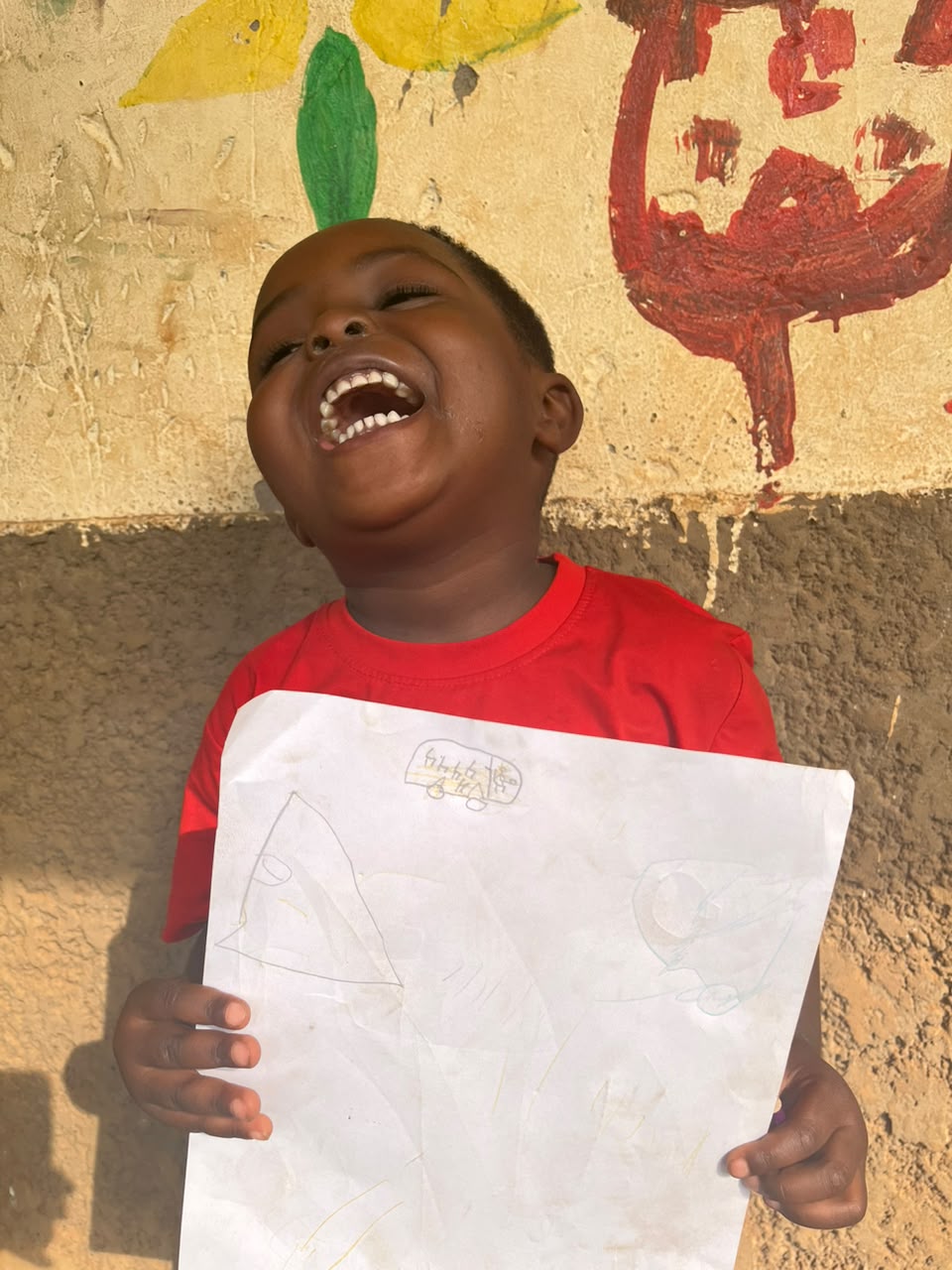 A boy at the Inzozi Learning Center laughing as he holds up his dream drawing